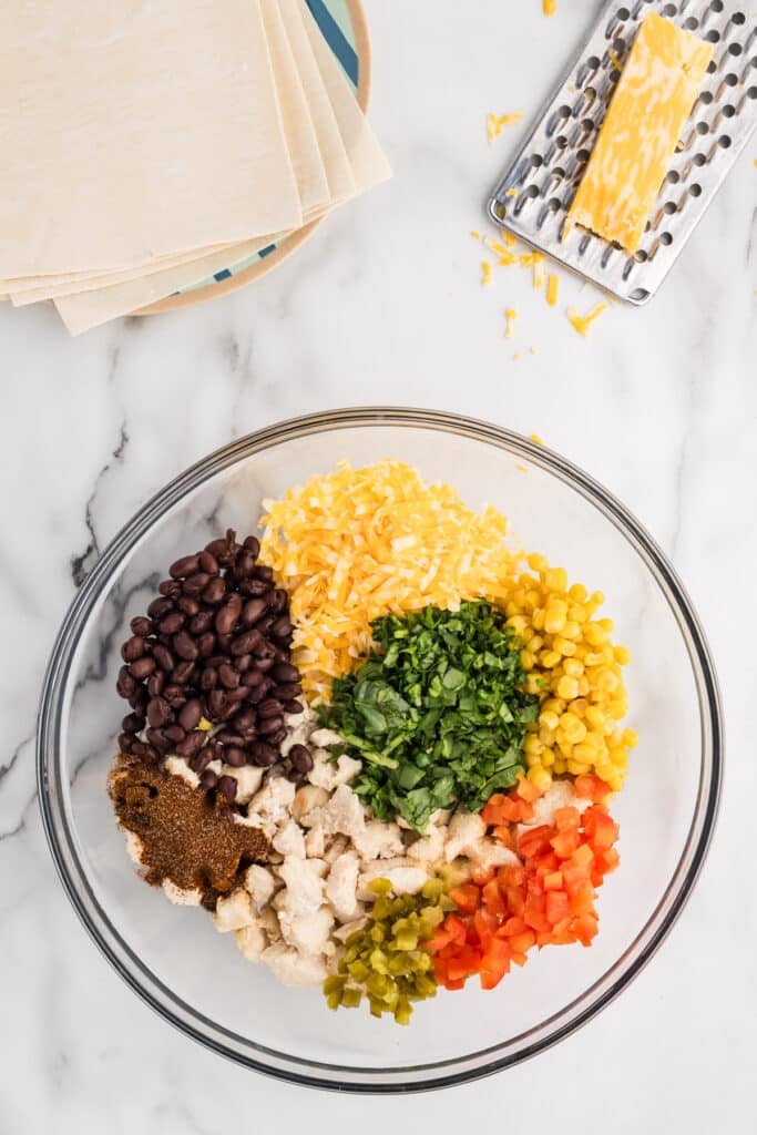 A large glass bowl showing individual ingredients for southwest egg roll filling.