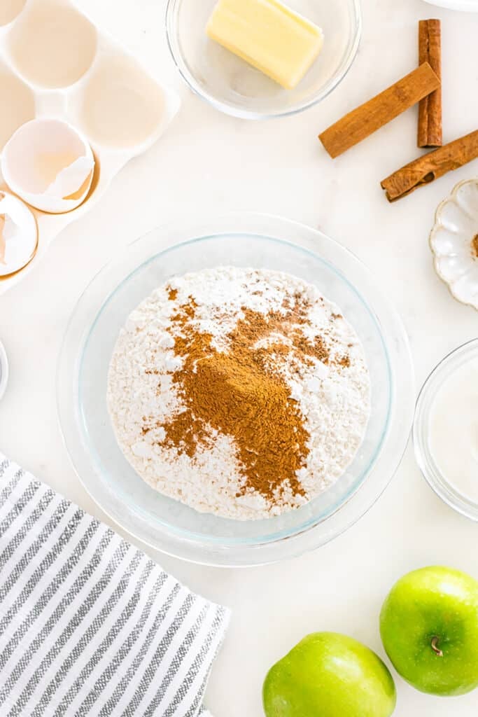 Flour and cinnamon in a glass bowl surrounded by baking ingredients.