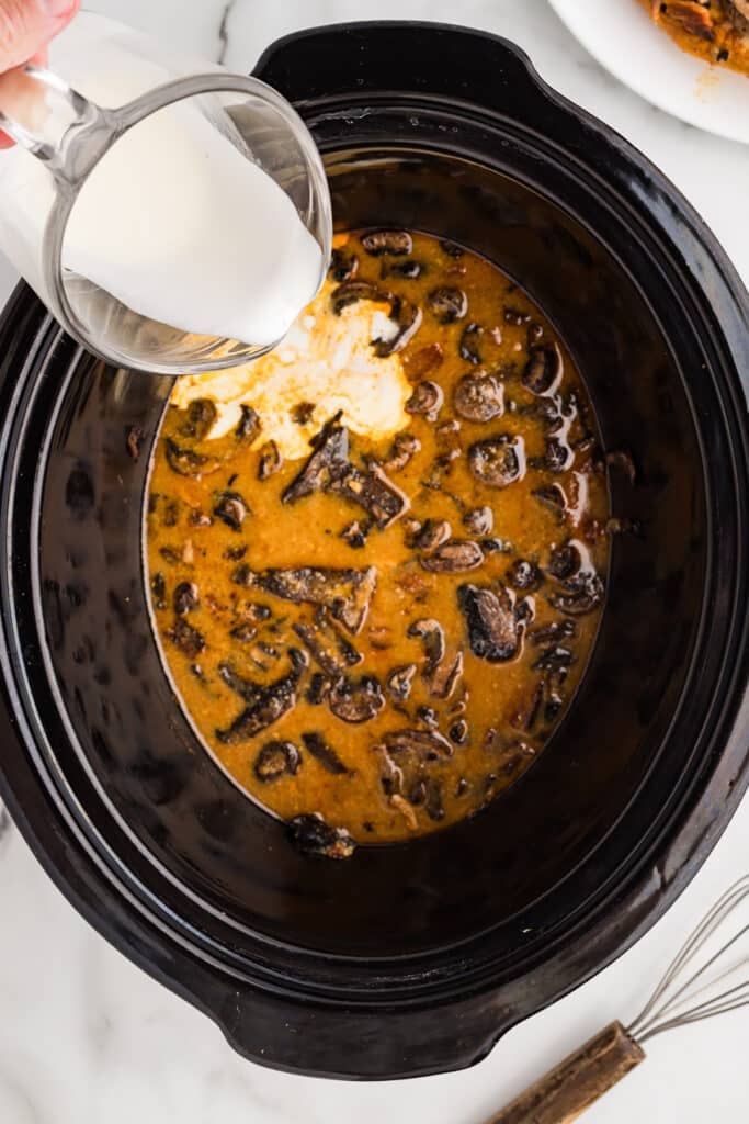 Cream being poured into a mushroom and sauce mixture in a slow cooker.