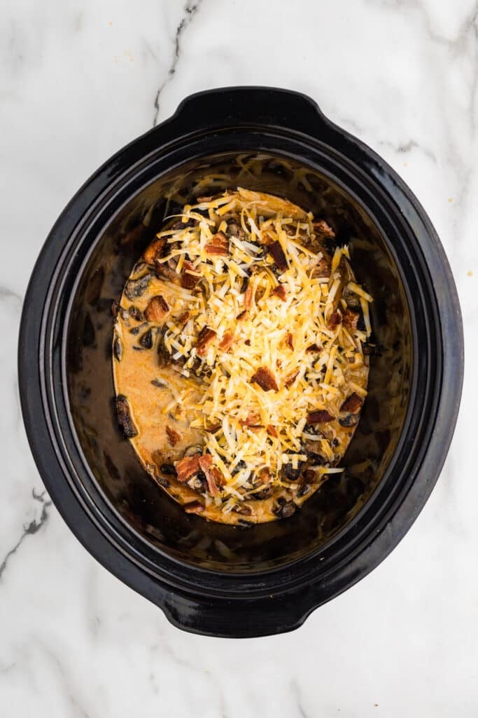 Slow cooker filled with chicken topped with melted cheese and bacon.