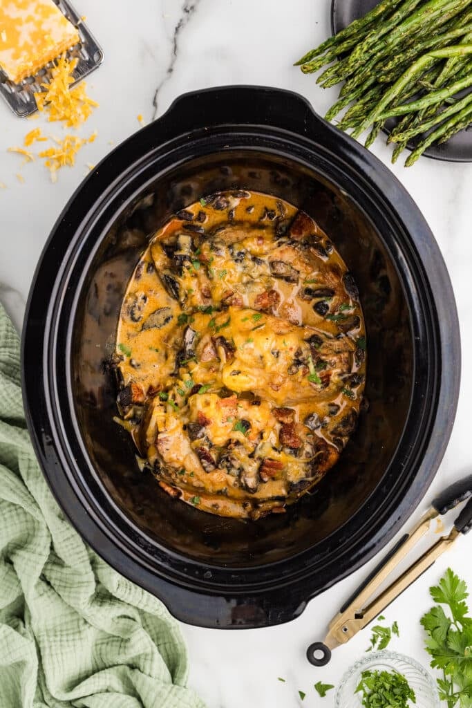 Cooked Alice Springs Chicken in a slow cooker topped with cheese and bacon.