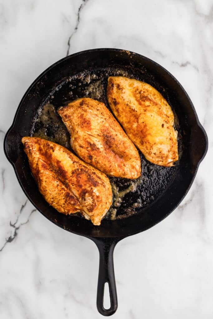 Seasoned chicken breasts cooking in a cast iron skillet.