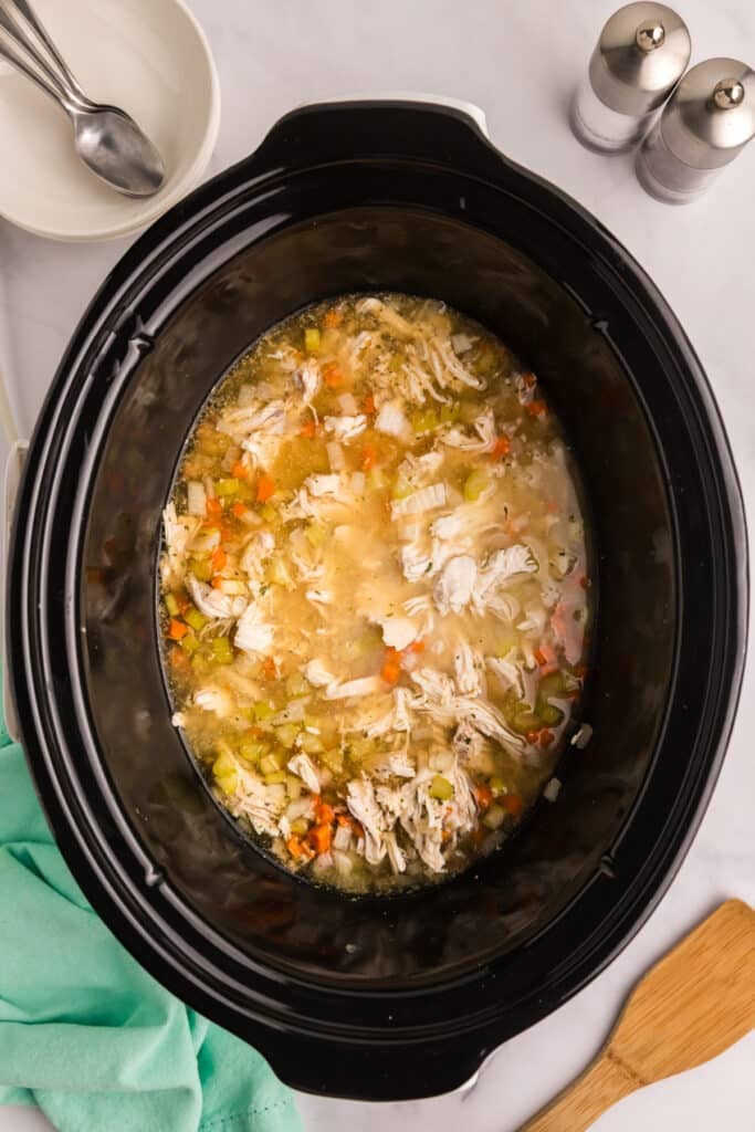 Shredded chicken and vegetables simmering in broth inside the slow cooker.