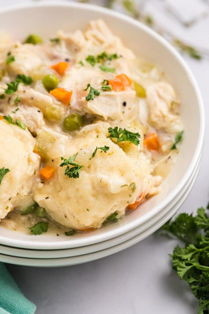 A bowl of creamy chicken and dumplings topped with chopped parsley.