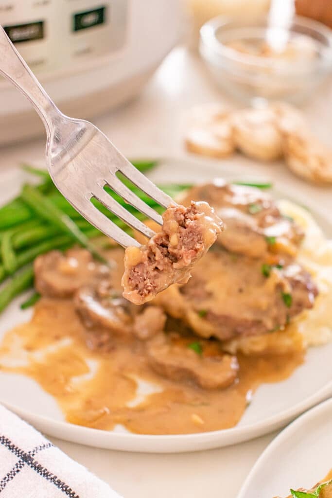 A fork holds a bite of cube steak over a plate with gravy and green beans.