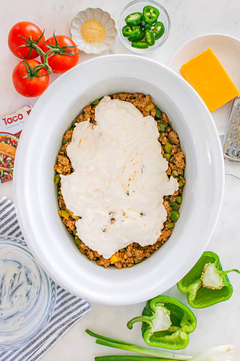 A layer of creamy mixture spread over cooked ground beef in a slow cooker.