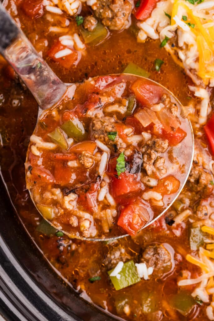 A ladle scooping stuffed pepper soup from a slow cooker.