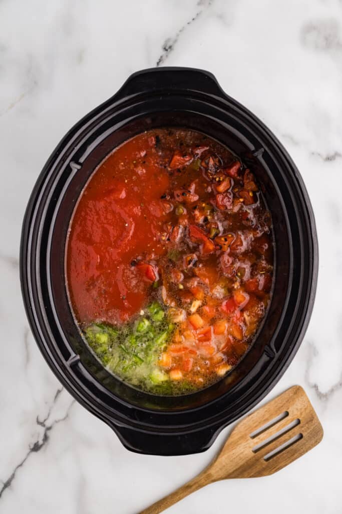 Ingredients for stuffed pepper soup layered in a slow cooker.
