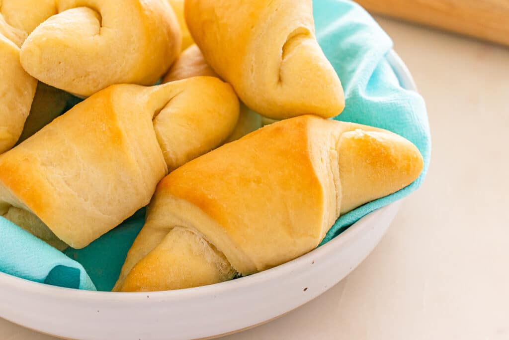 Crescent rolls nestled in a white bowl lined with a turquoise cloth.