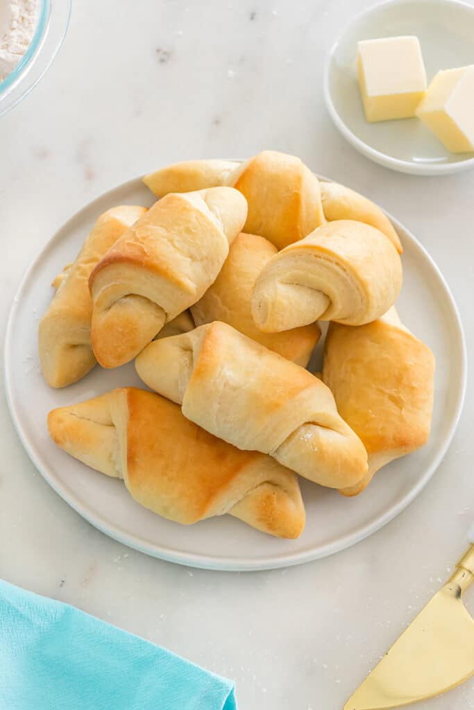 A plate of freshly baked crescent rolls on a marble surface with butter beside it.