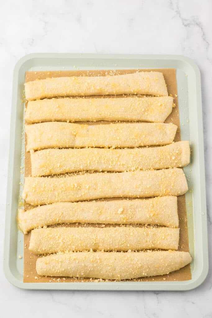 Breadsticks covered in butter and parmesan on a baking sheet.
