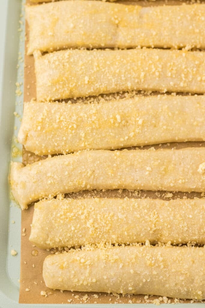 Unbaked breadsticks lined on a baking sheet.