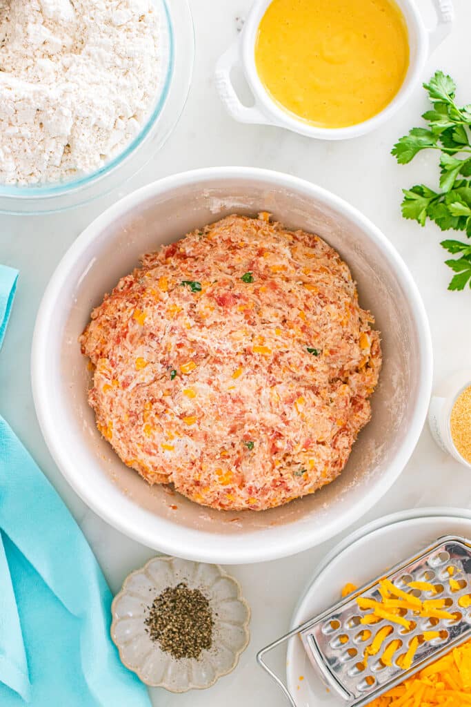 A bowl of blended sausage ball dough with bits of cheese and herbs.