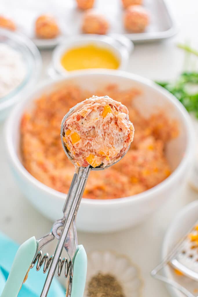 A cookie scoop holding a ball of raw sausage and cheese mixture.