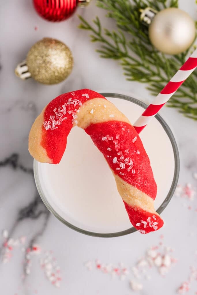 Candy cane–shaped cookie resting on the rim of a glass of milk.