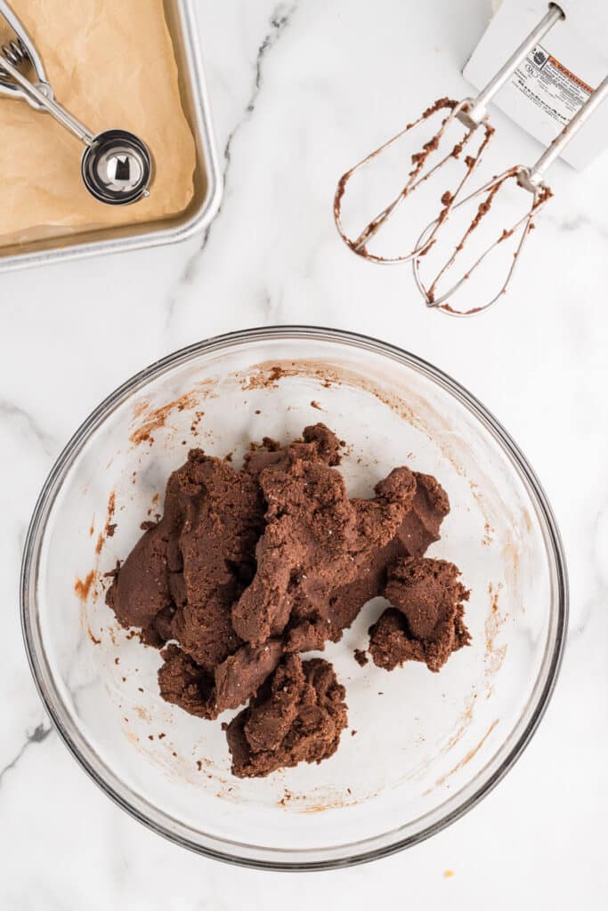 A glass bowl filled with chocolate cookie dough on a marble surface.