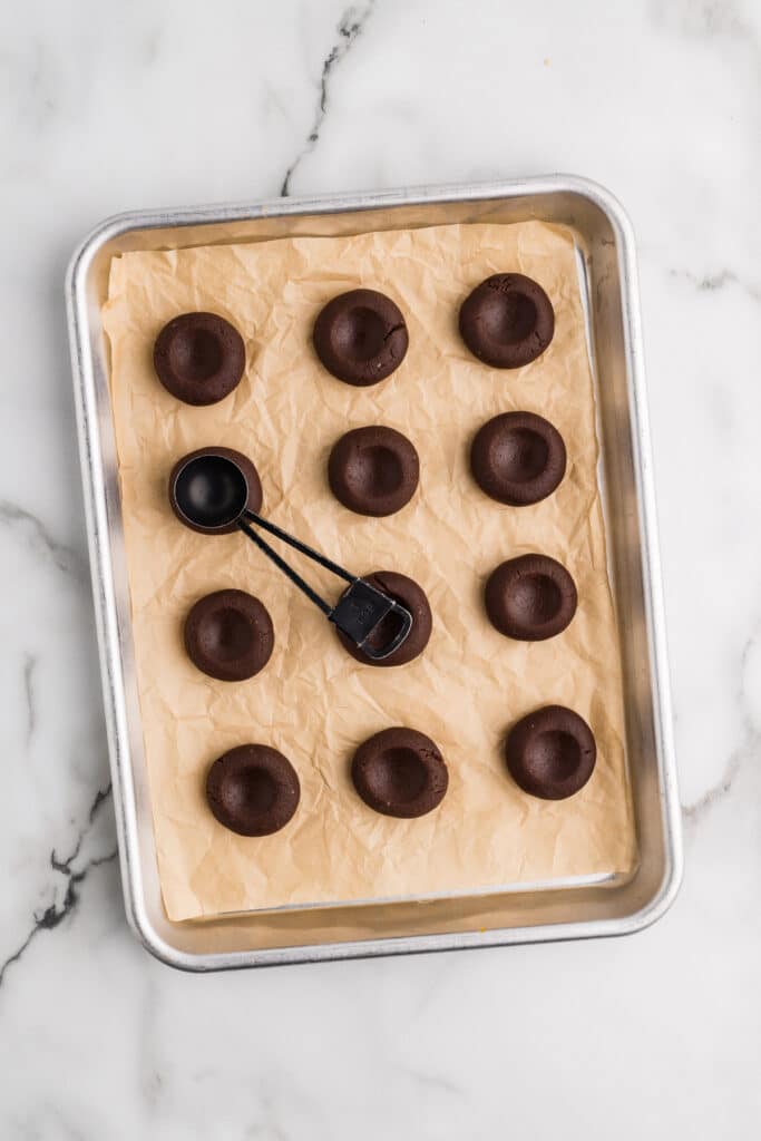 Unbaked chocolate cookies with indents on a parchment-lined baking sheet.