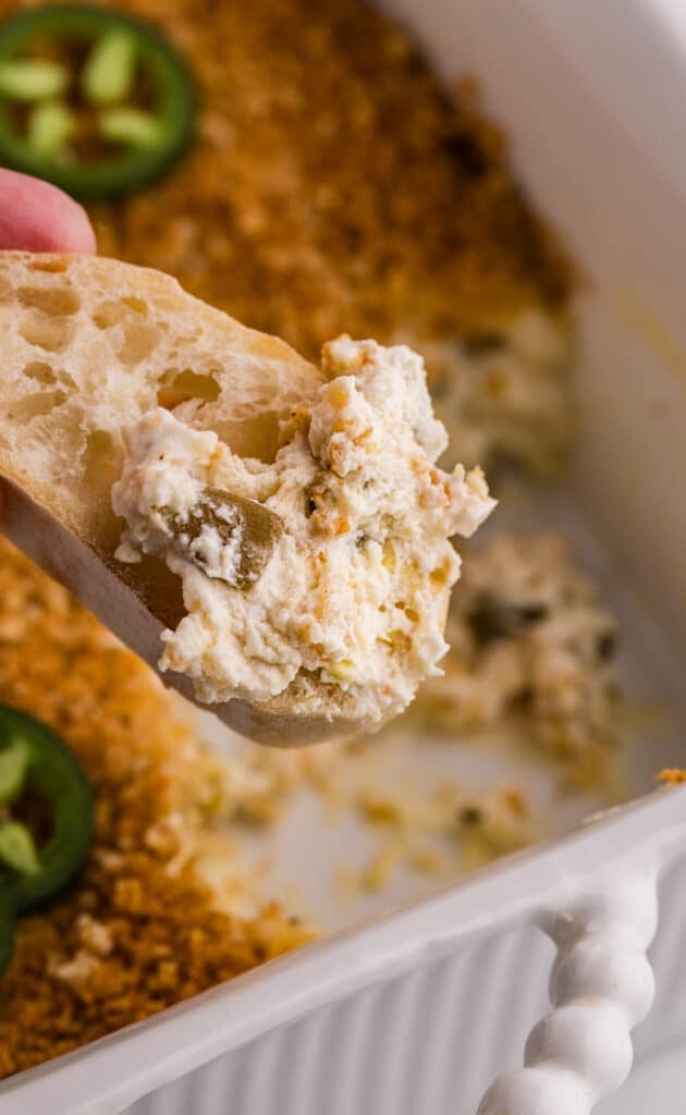 Slice of bread dipped into creamy jalapeño popper dip.