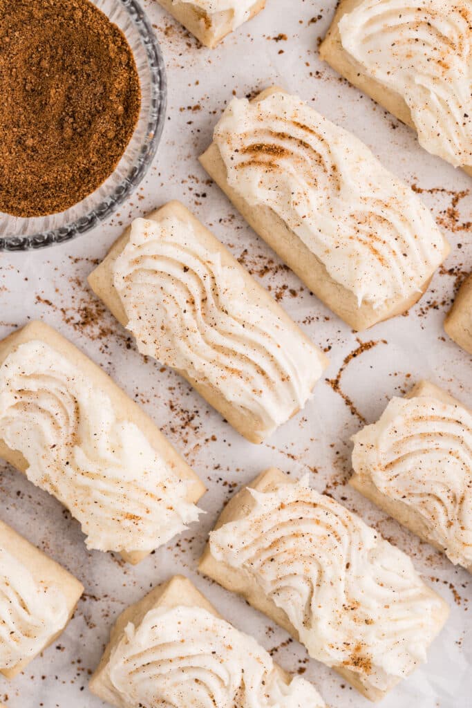 Frosted rectangular cookies sprinkled with nutmeg arranged on parchment beside a bowl of ground spice.