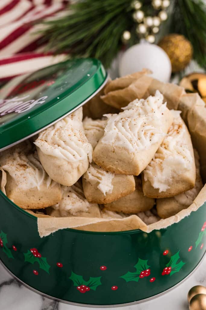 Frosted cookies stacked inside a green holiday tin lined with parchment paper.