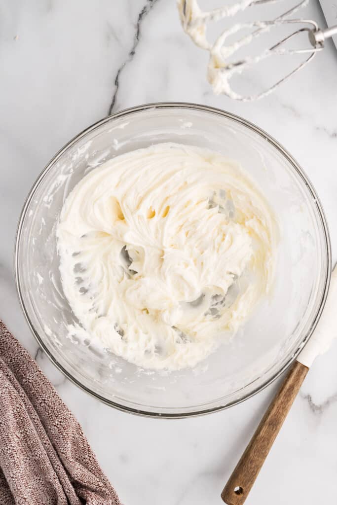 A glass bowl filled with whipped white frosting on a marble surface.