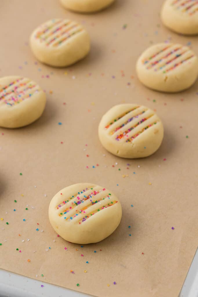 Unbaked round cookie dough topped with rainbow sprinkles on parchment paper.