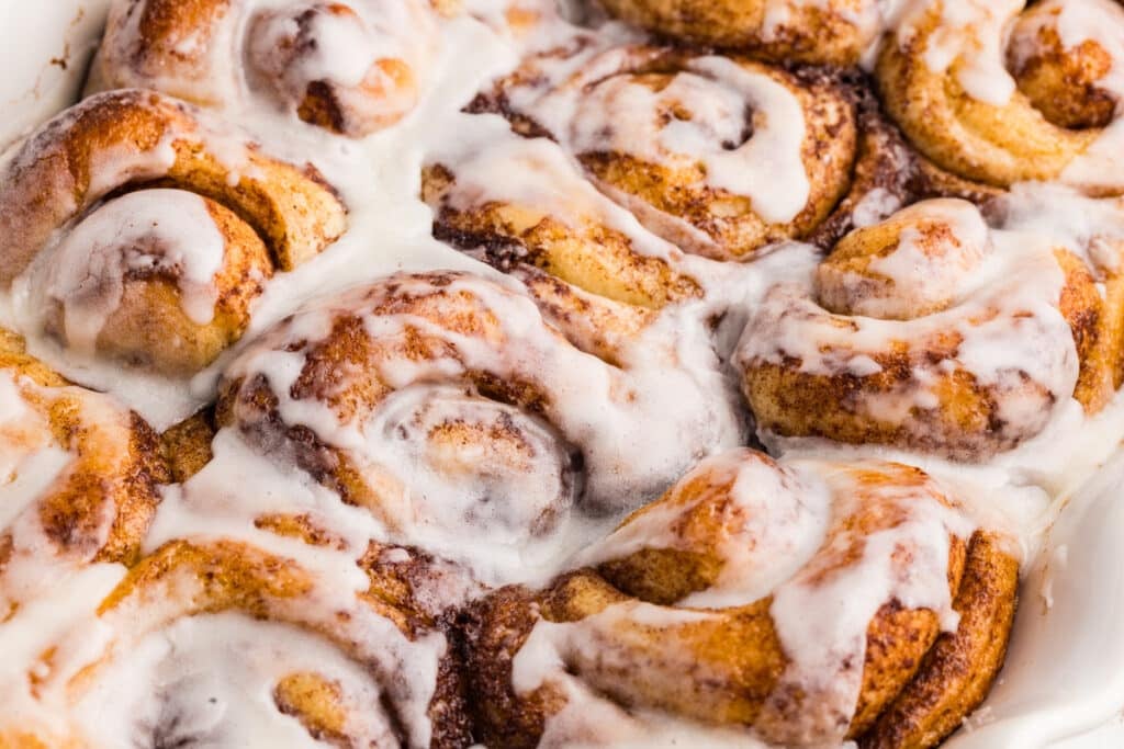 Close-up of baked cinnamon rolls packed tightly together, topped with glossy white icing melting into the spirals.