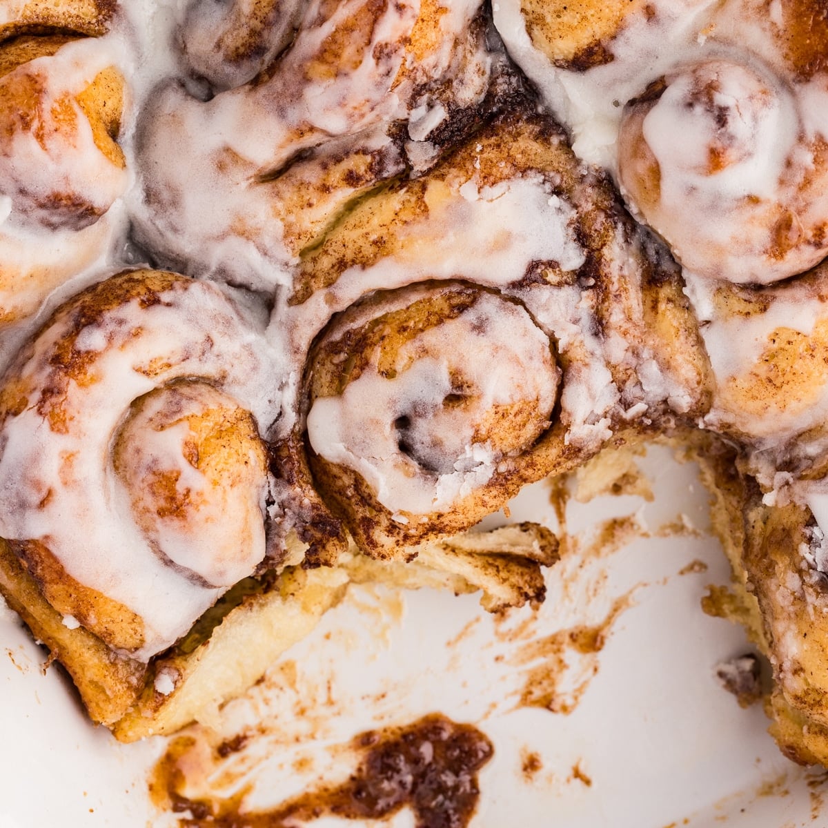 Baking dish of cinnamon rolls with one roll removed.