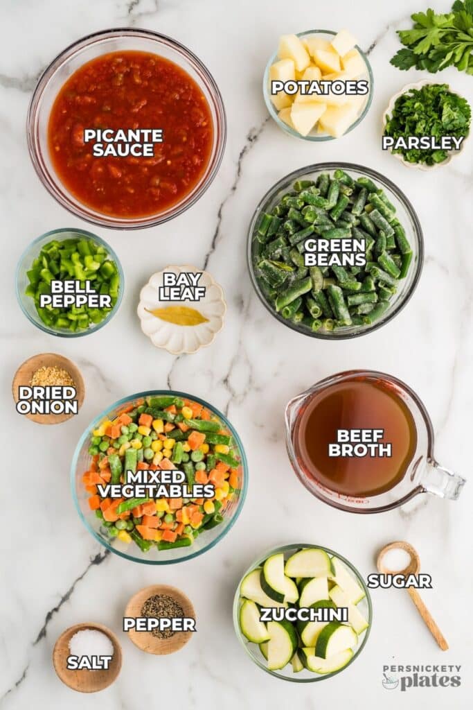 Labeled ingredients for vegetable soup arranged on a marble surface.