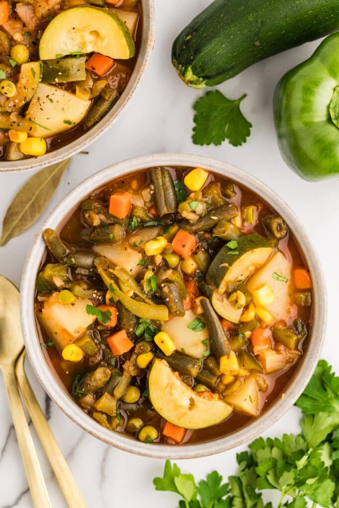 Two bowls of vegetable soup with potatoes, zucchini, green beans, carrots, and corn.