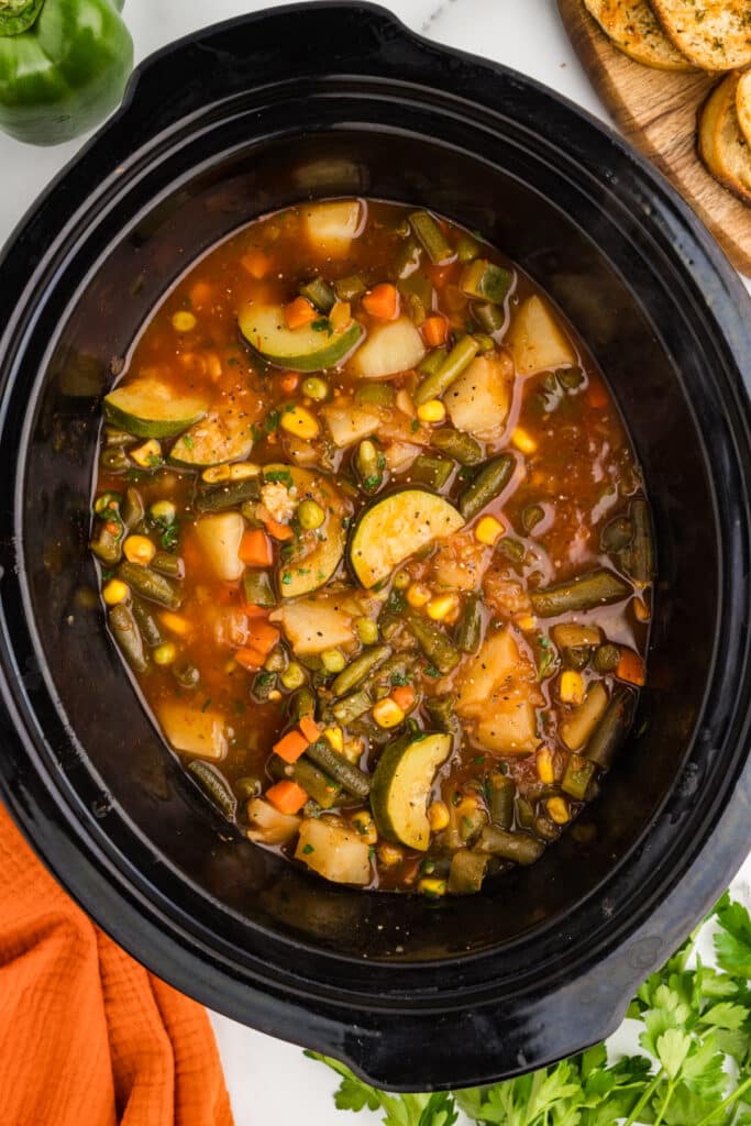 Vegetable soup cooking inside a black slow cooker.