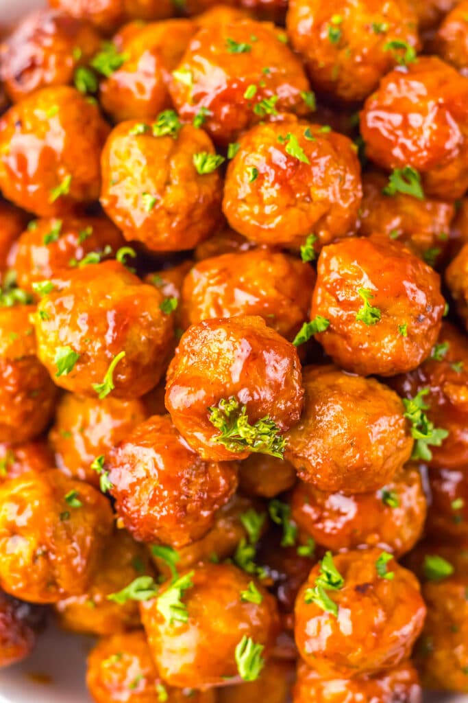 Close-up of glossy meatballs coated in sauce and garnished with chopped parsley.