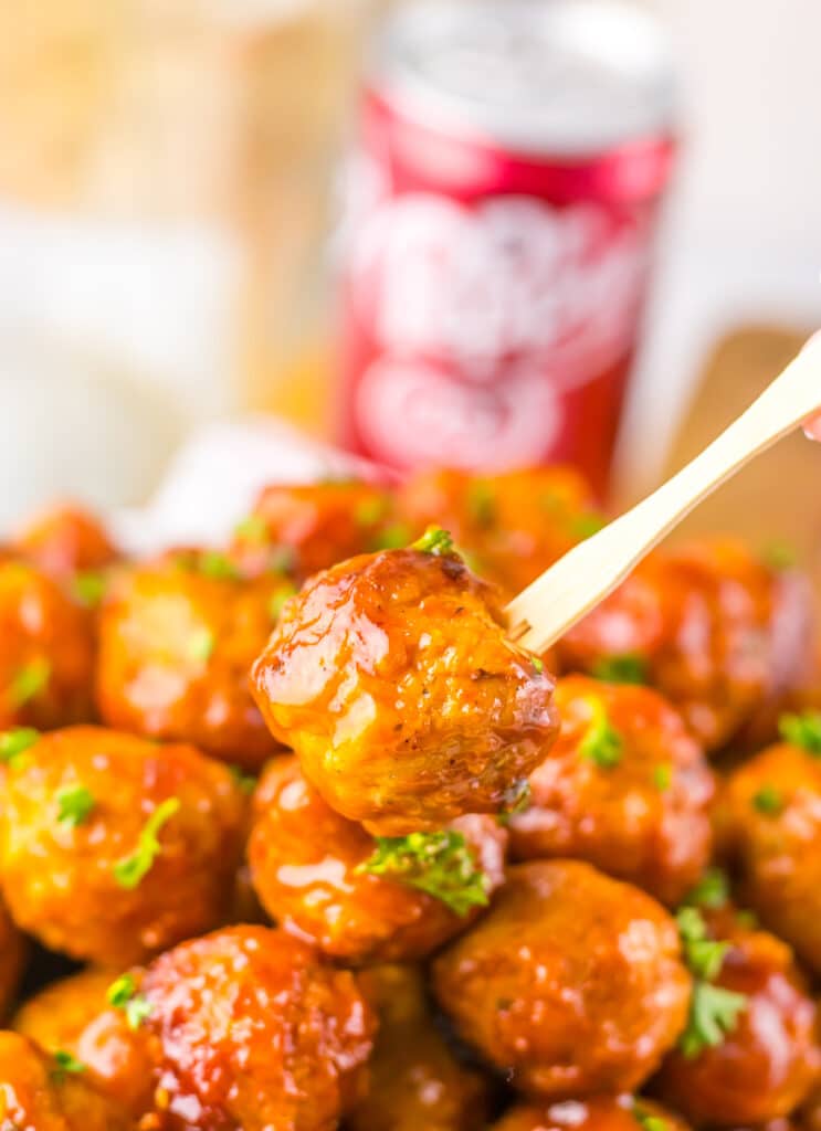 Glazed meatball on a wooden toothpick with a blurred Dr. Pepper can in the background.