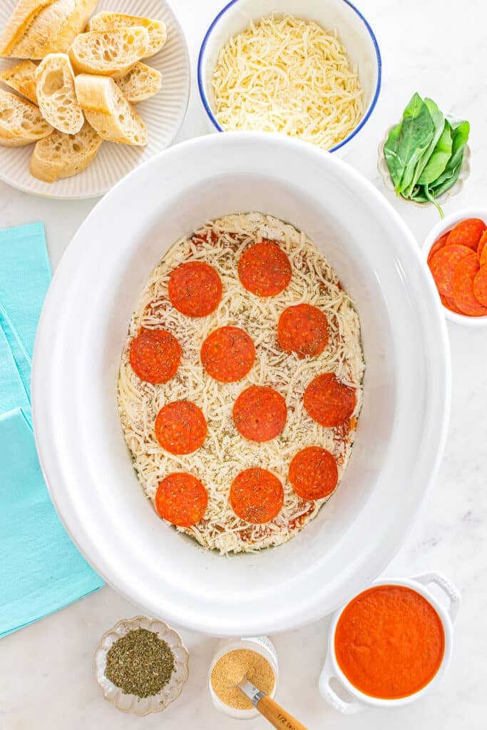 Uncooked pizza dip layered with cheese and pepperoni in a crockpot.