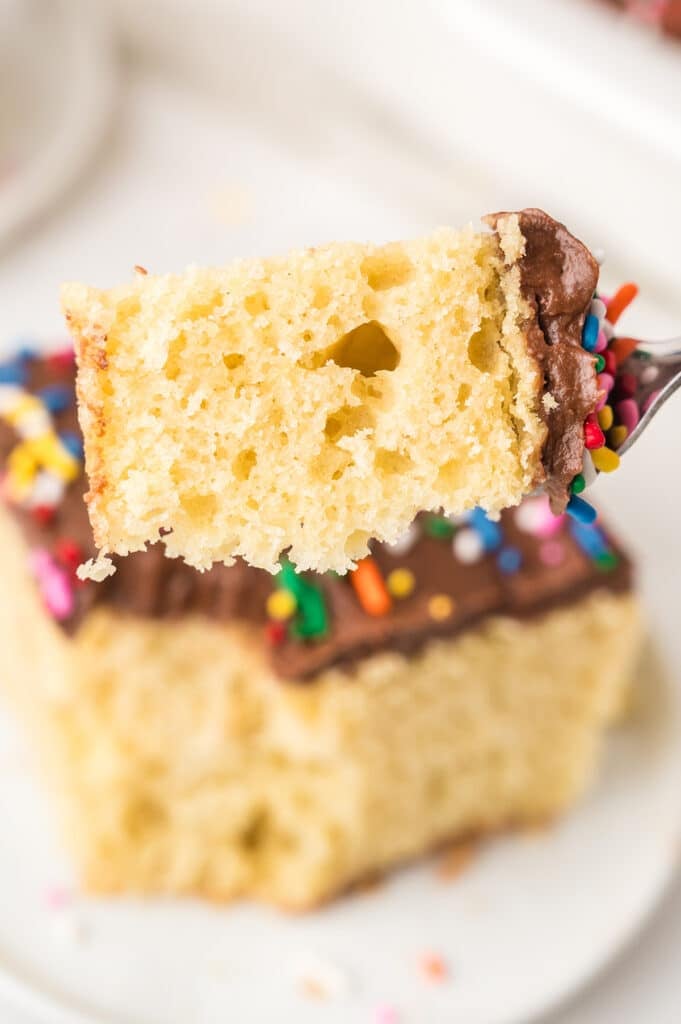 Fork holding a bite of yellow cake with chocolate frosting and sprinkles.