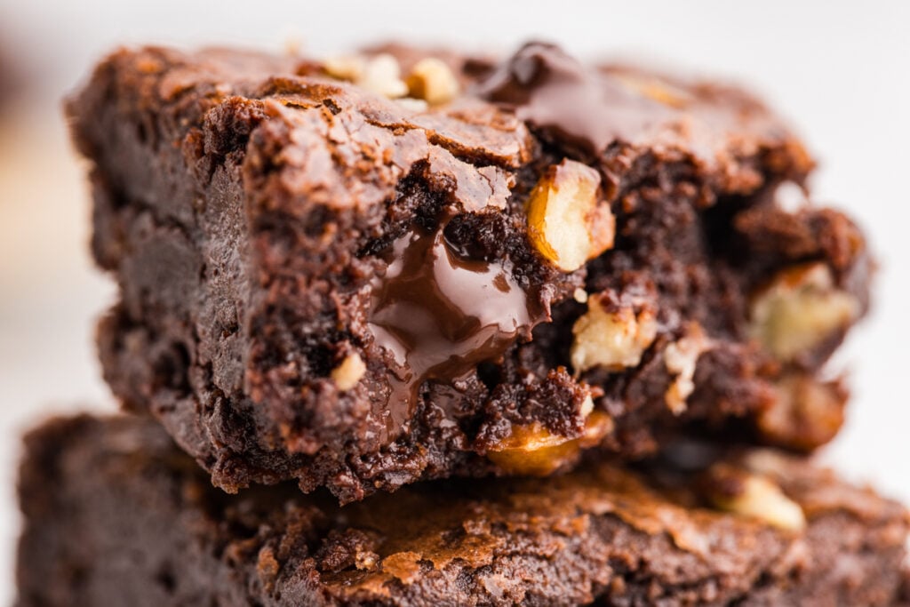 Close-up of stacked chocolate brownies with pecans and melted chocolate in the center.